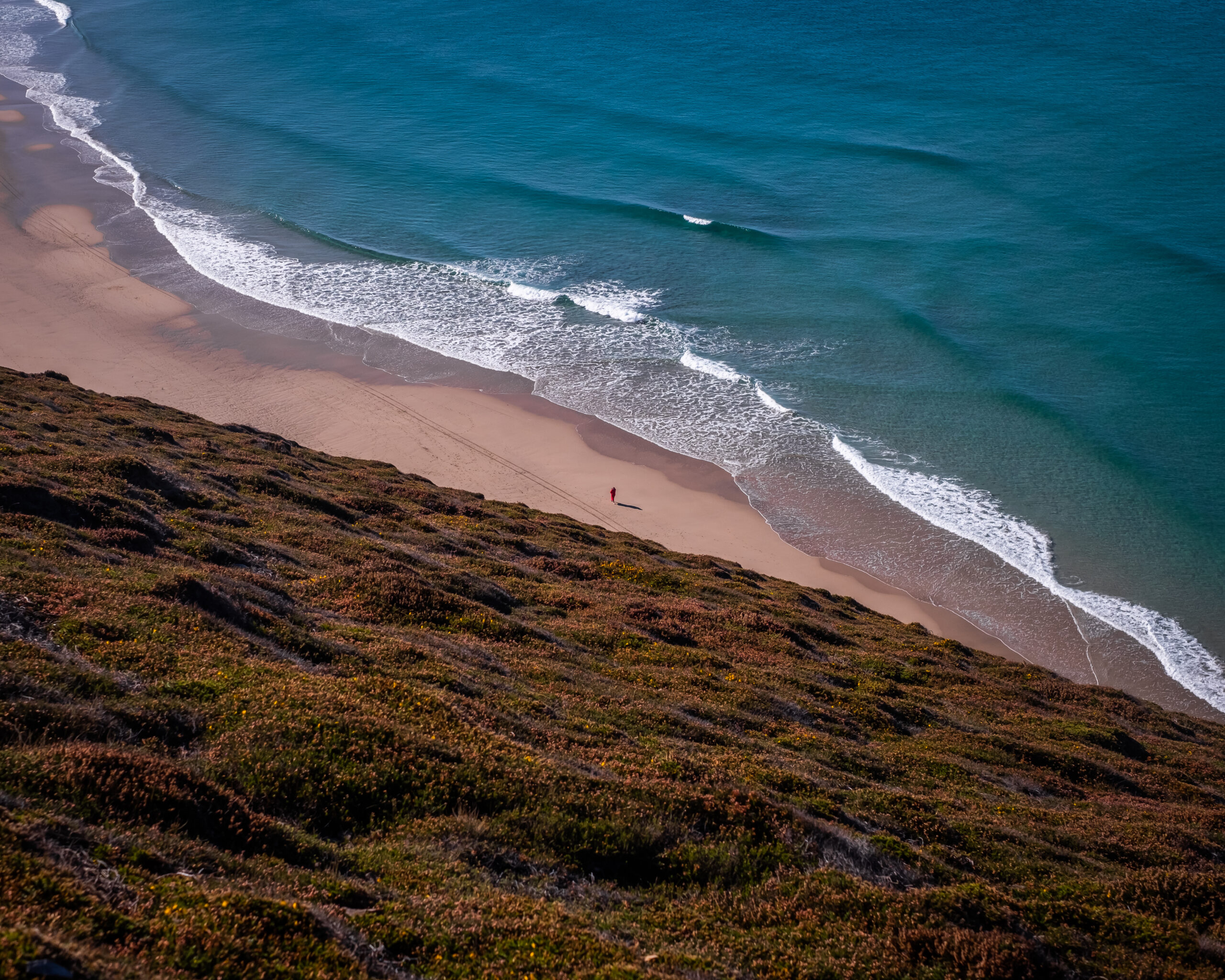 A birds eye view of a beach, with a lone person standing in the middle of the frame.